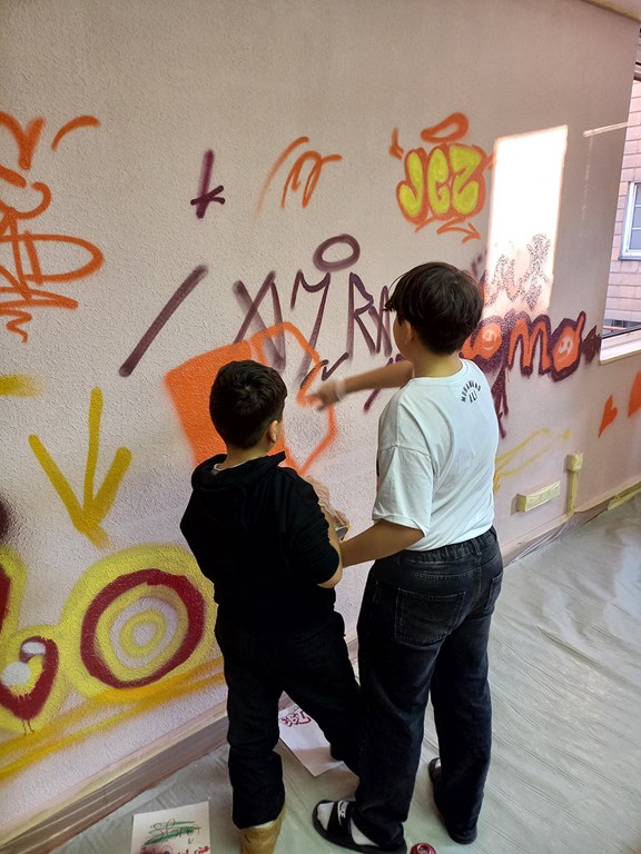 Zwei Kinder, die etwas an eine Wand sprayen