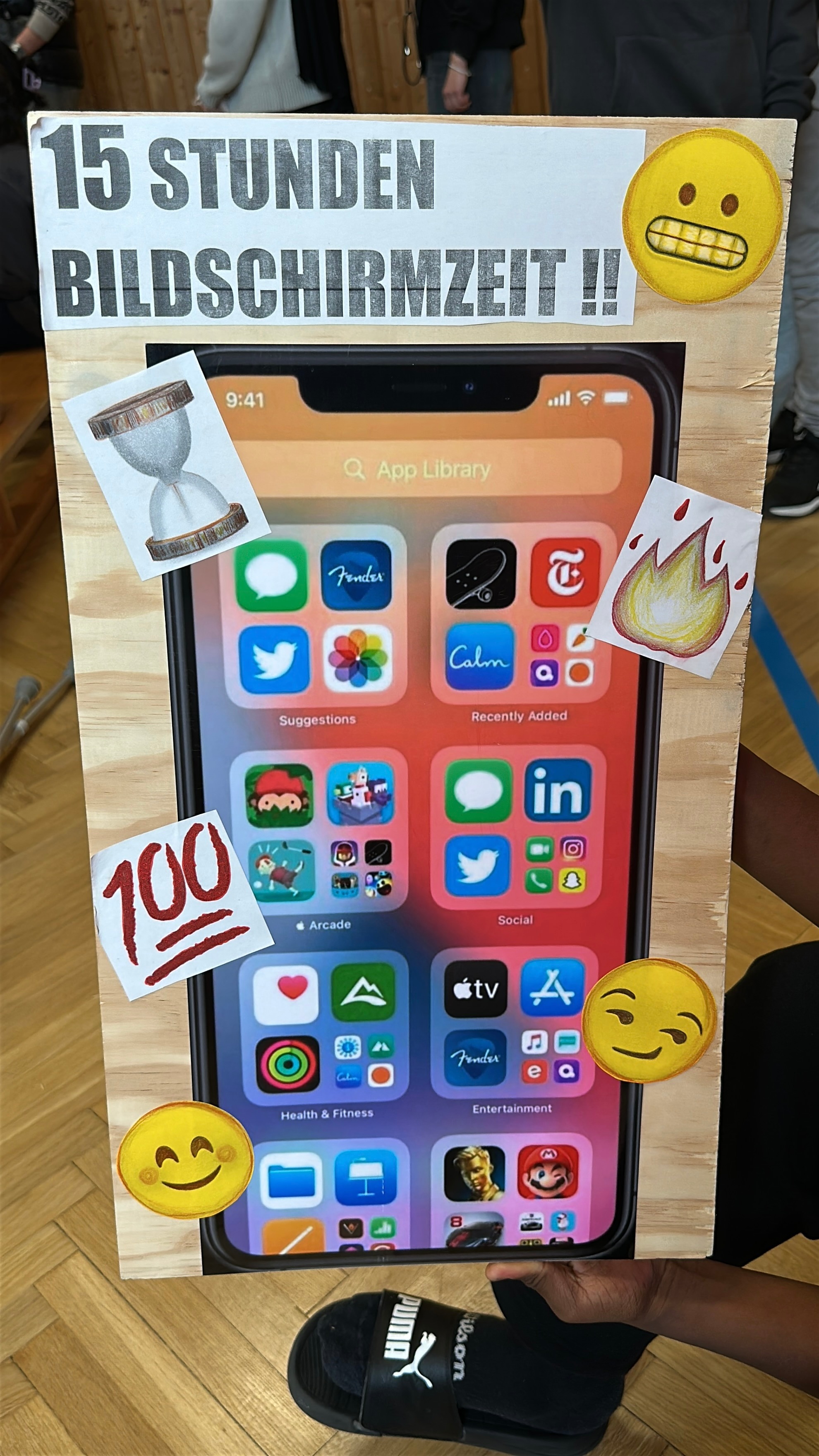 Plakat mit einem Handy aufgedruckt. In dramatischer Gestaltung ist der Text "15 Stunden Bildschirmzeit" zu lesen