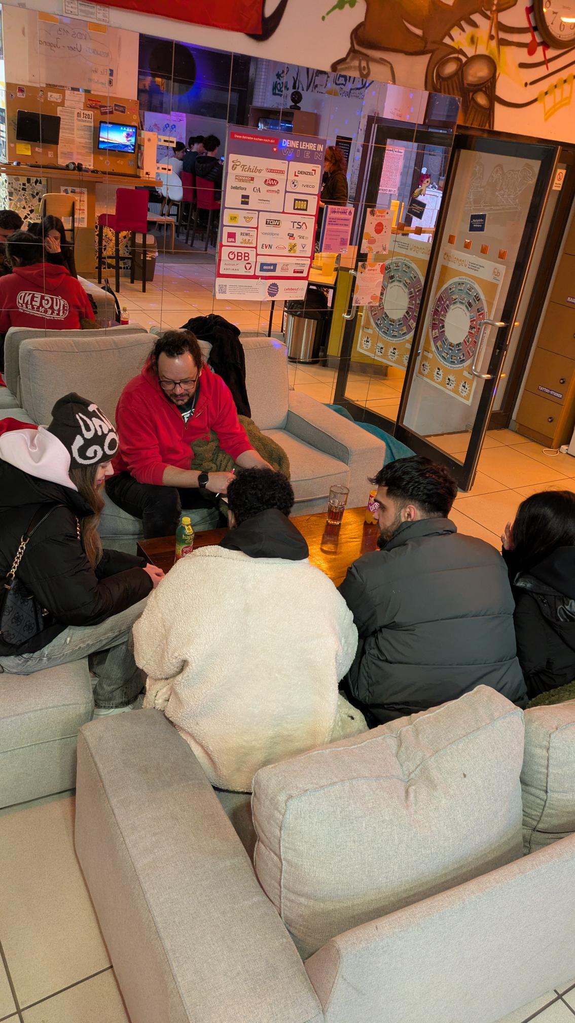 Jugendliche und Jugendarbeiter sitzen im Kreis auf Couches, dahinter Spiegelwand zu sehen