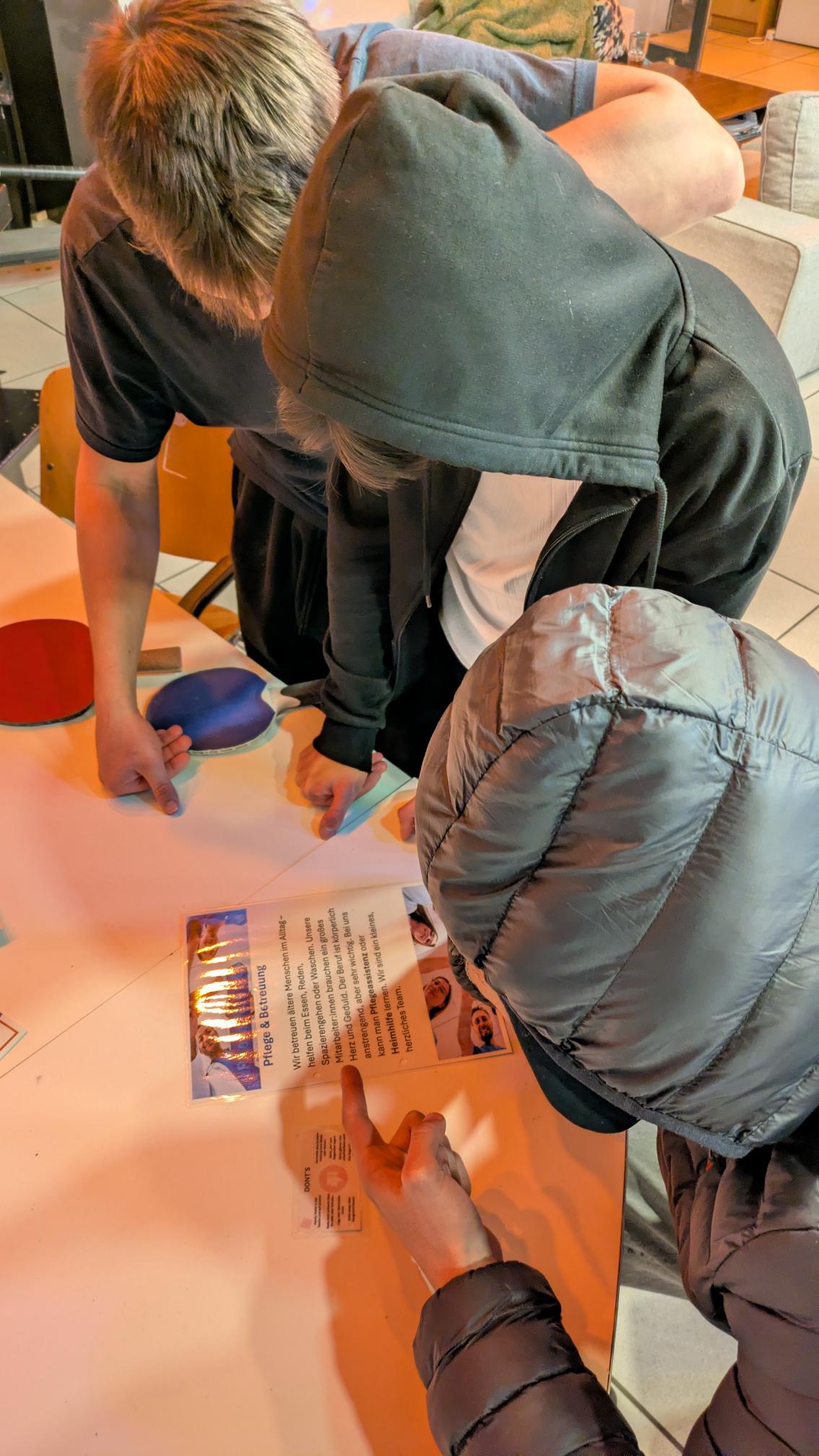 Drei Jugendliche lesen ein Informationsblatt über den Arbeitsbereich Pflege und Betreuung