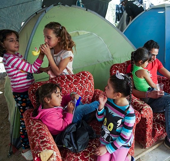 Mehrere Mädchen spielen in Mitten eines Zeltlagers, wo auch ein junger Mann sitzt, der zu Boden starrt