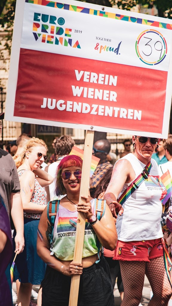 Eine Jugendarbeiterin steht bei der Europride mit dem großen Verein Wiener Jugendzentren-Paradenschild.