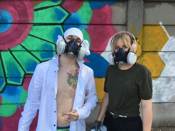 zwei junge Menschen mit einer Sauerstoffmaske vor einer Graffitiwand