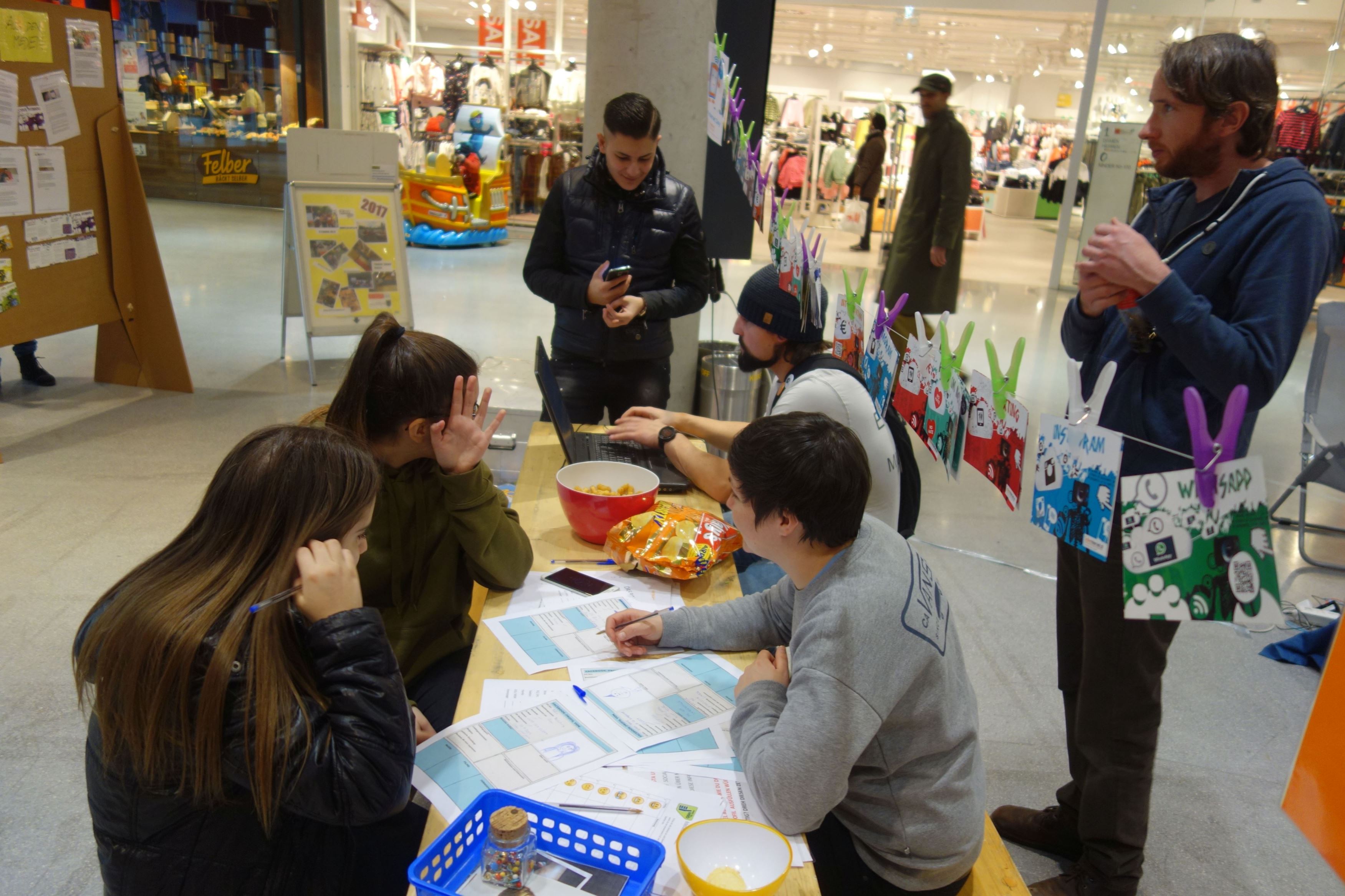 Jugendliche sitzen auf einer Bank mit Tisch in einem Einkaufszentrum