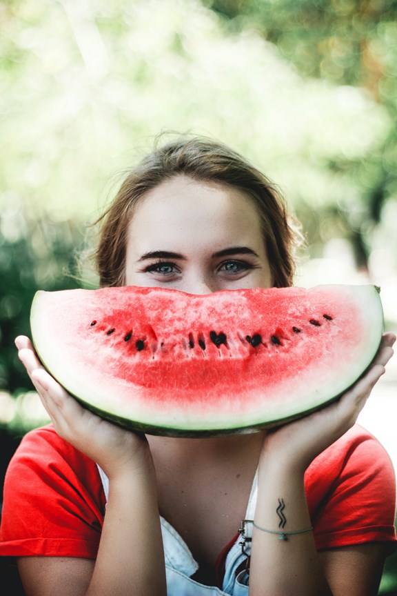 Eine Frau hält eine Wassermelone vor ihr Gesicht.
