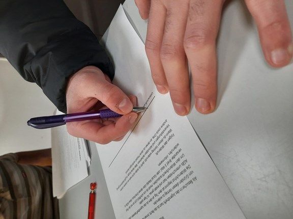 Eine Hand hält einen Stift und schreibt etwas auf ein Blatt Papier.