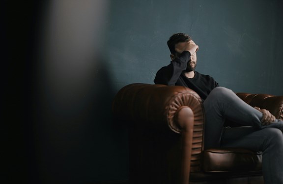 Ein Mann mit Hand vor dem Gesicht auf einer Couch