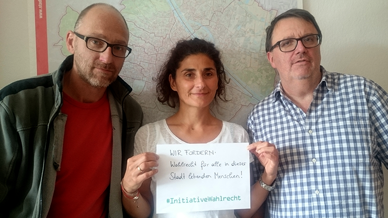 Mitarbeiter:innen des Verein Wiener Jugendzentren halten ein Blatt Papier mit einem Statement vor sich: Wir fordern Wahlrecht für alle in dieser Stadt lebenden Menschen!