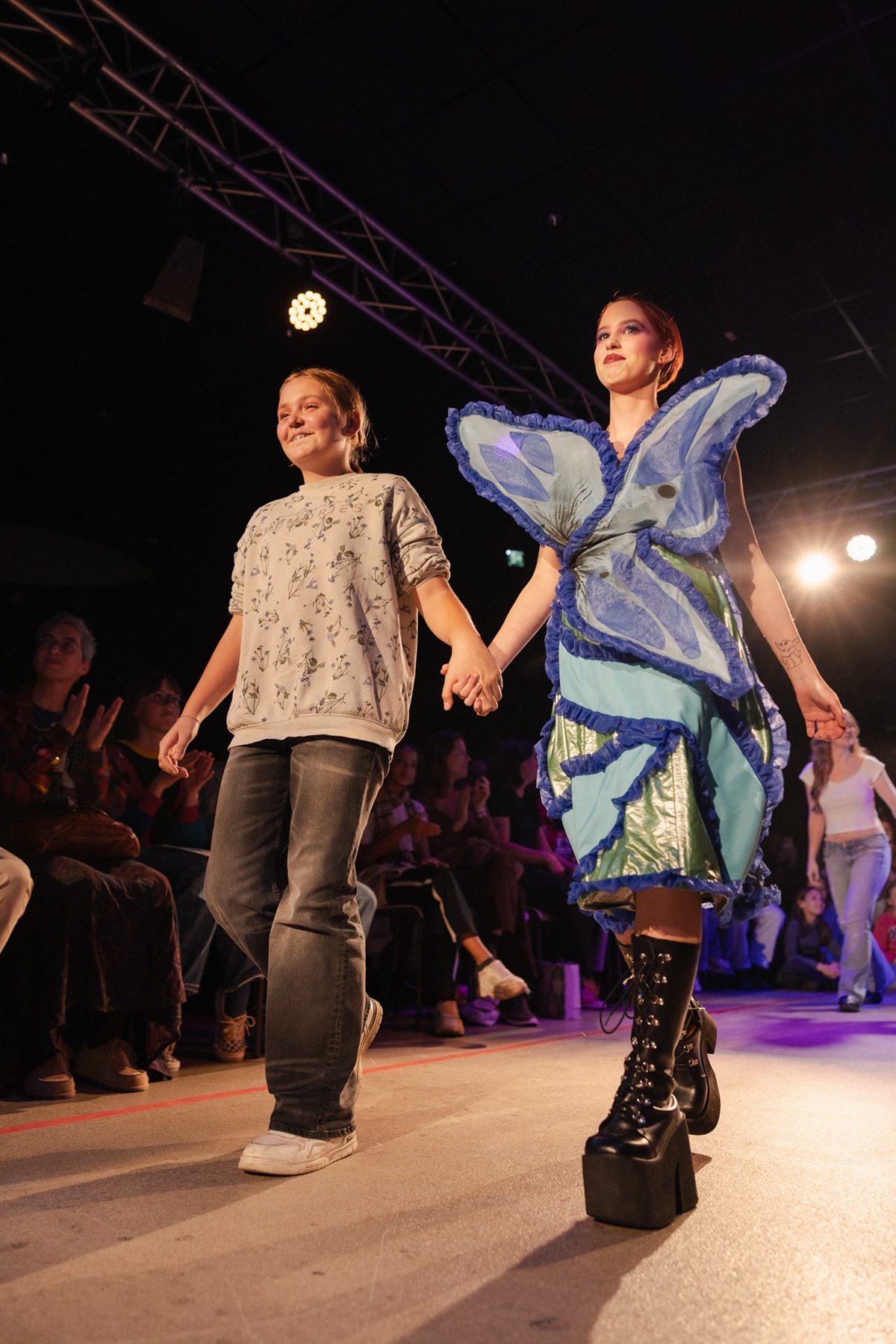 Model mit bunten Outfit und Kind an der Hand am Laufsteg