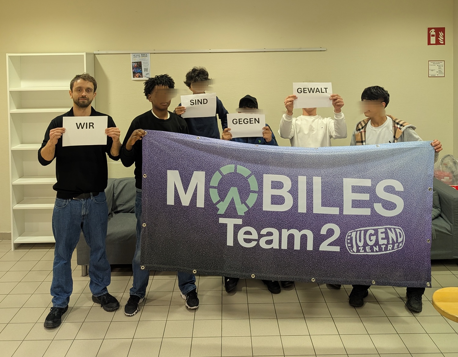 Gruppenfoto von Jugendlichen mit Zetteln in der Hand "Wir sind gegen Gewalt" und halten Mobiles Team 2 Banner hoch