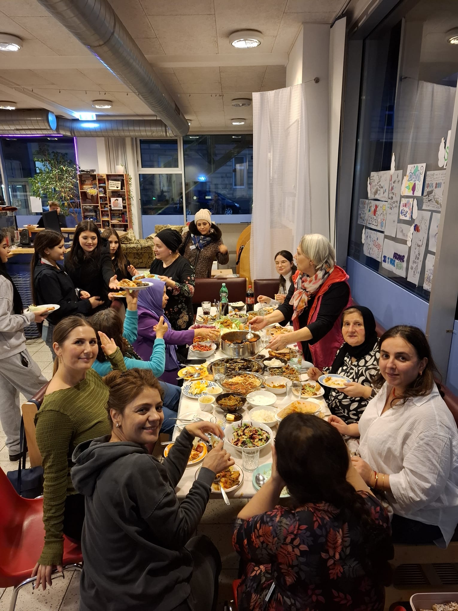 Gruppenfoto von Frauen* rund um Tisch mit verschiedenen Speisen