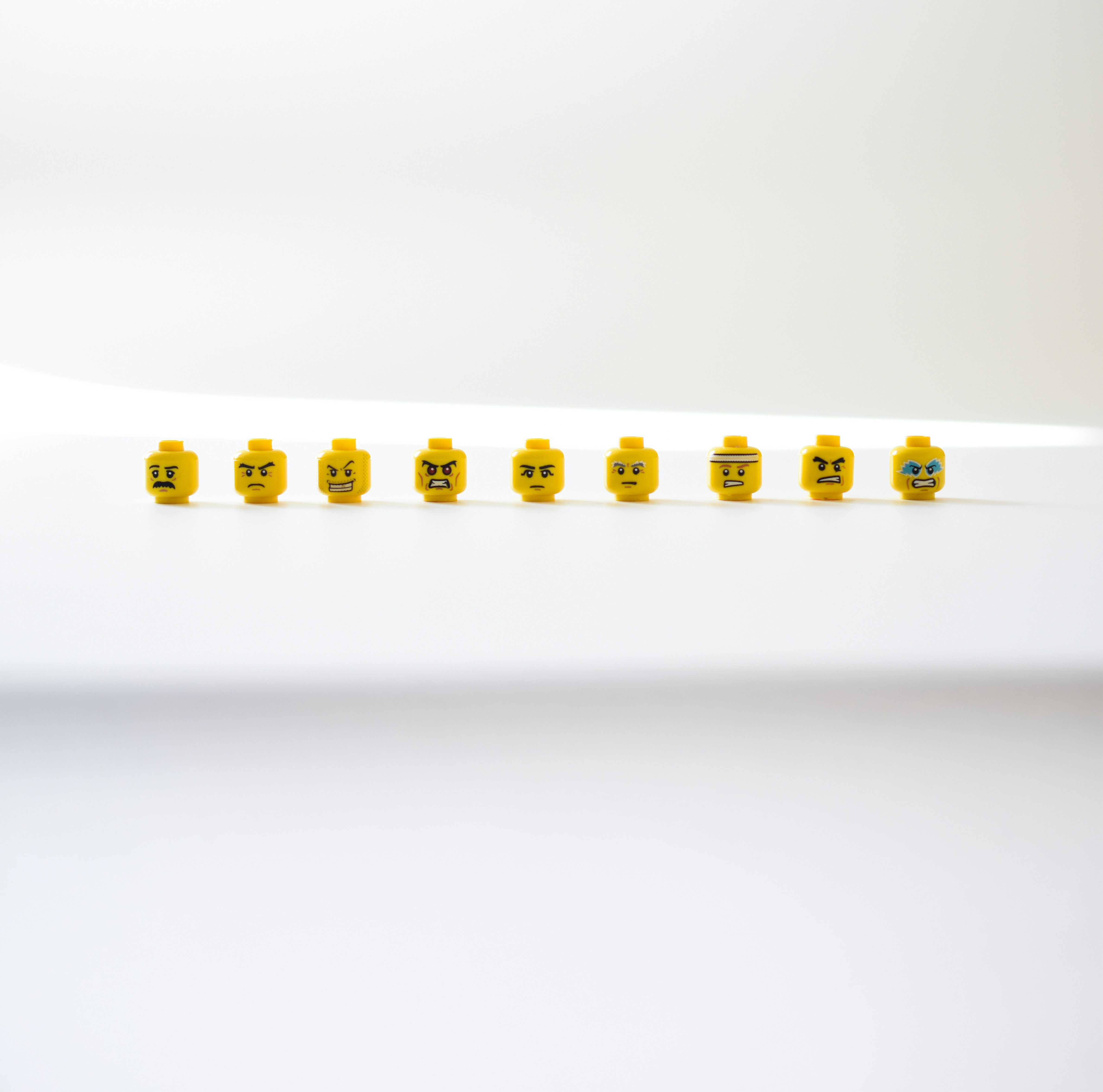 9 Lego-Köpfe mit verschiedenen, wütenden Mimik vor einem weißen, neutralen Hintergrund