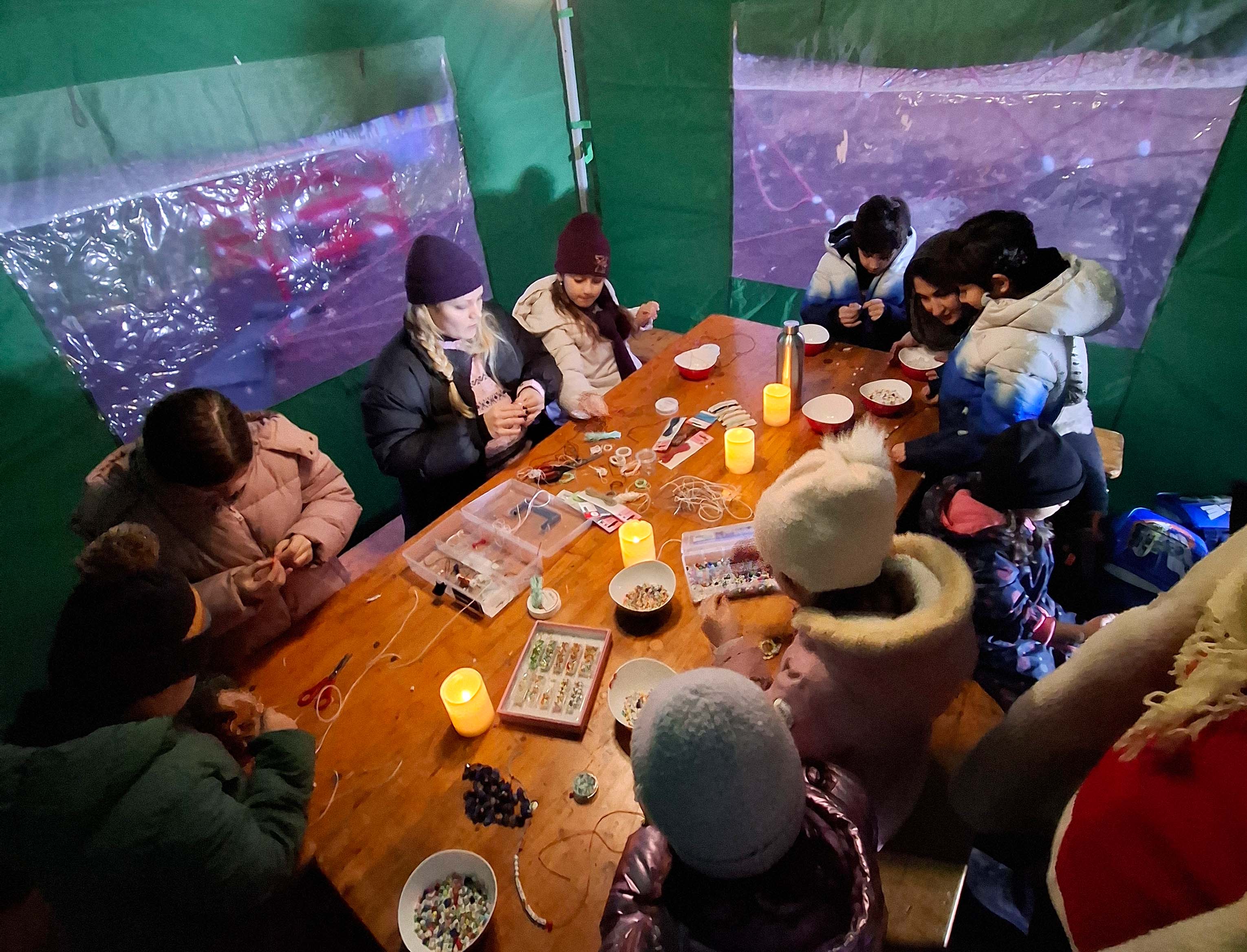 Kinder sitzen gemeinsam mit Jugendarbeiter:innen im Zelt des Jugendzentrums Hirschstetten und basteln.