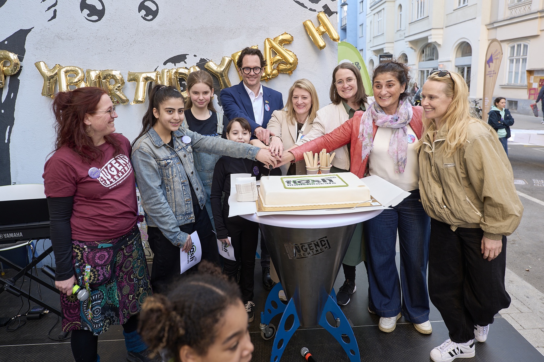 Mädchen* und Erwachsene schneiden auf der Bühne gemeinsam Torte an