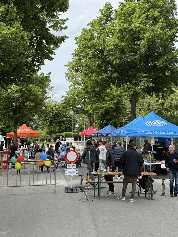 abgesperrte Straße, Zelte, Tische und Bänke mit Personen zu sehen