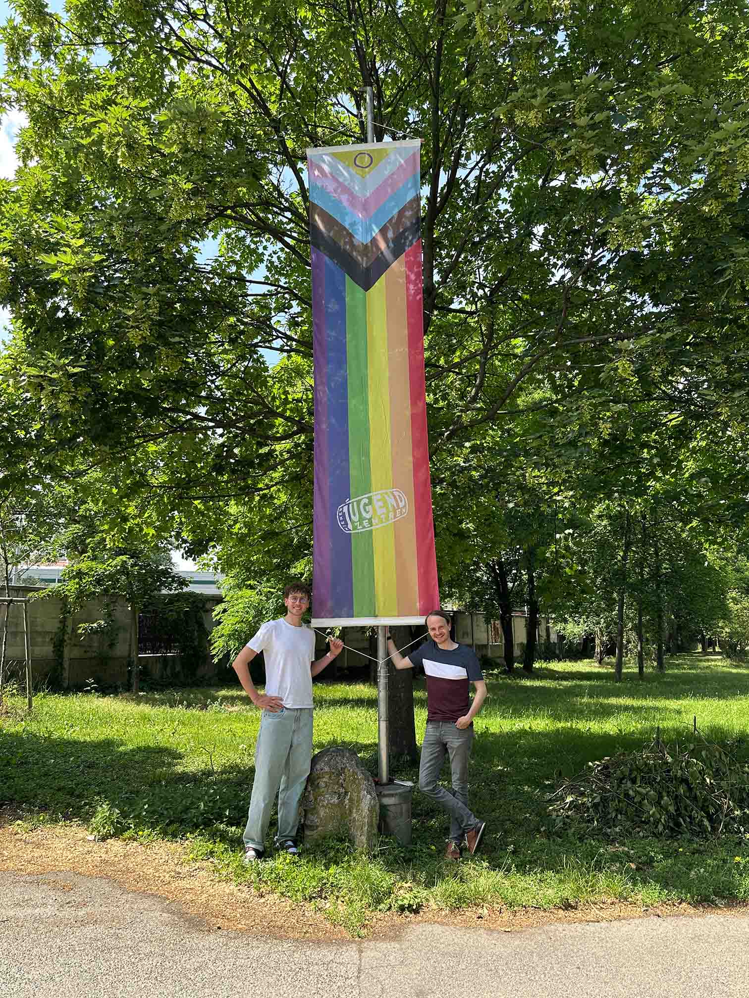 Zwei Mitarbeiter des Vereins hissen Progress-Pride-Flagge beim Eingang zur zentralen Geschäftsstelle des Vereins Wiener Jugendzentren.