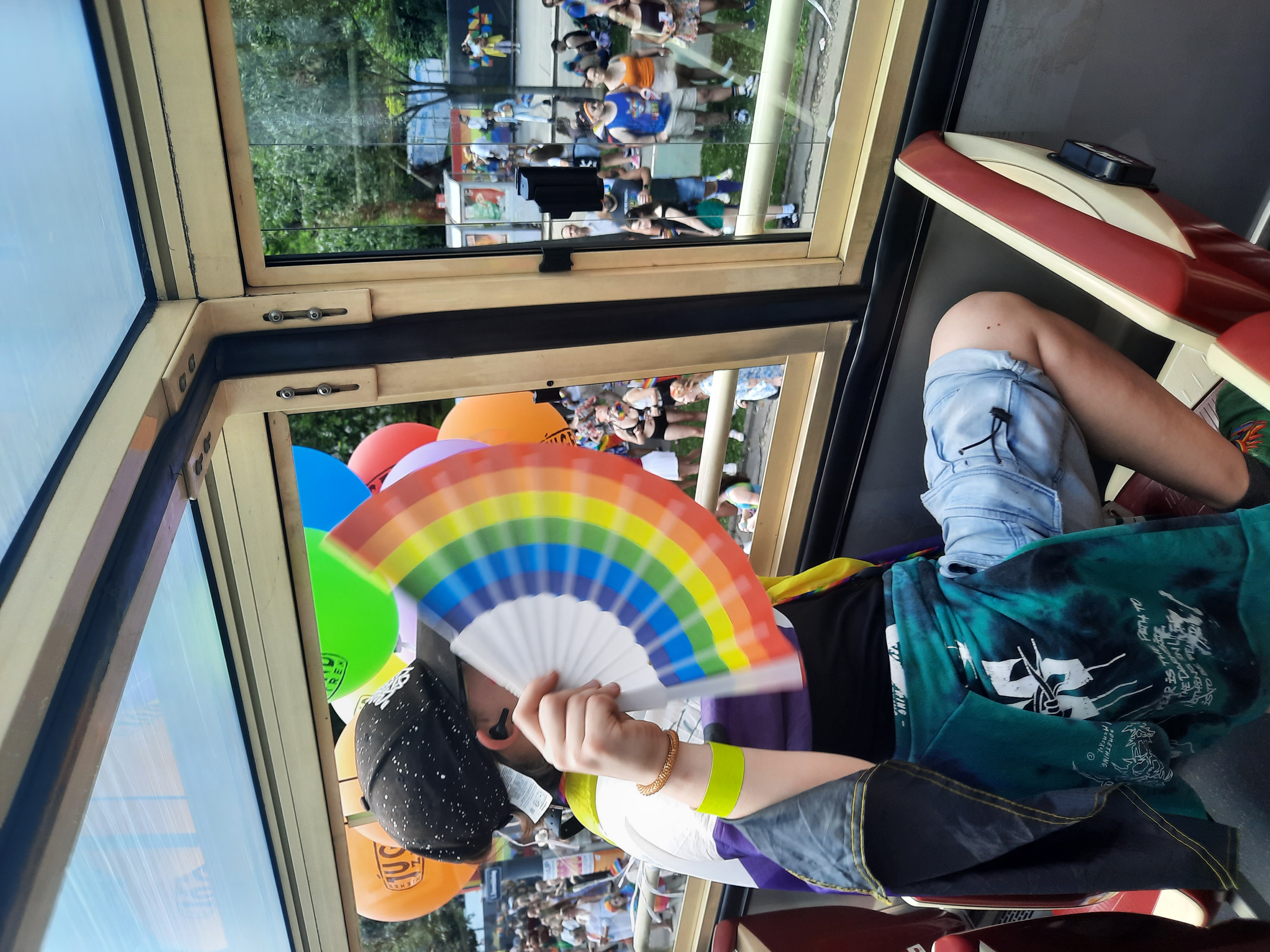 Jugendliche Person mit Regenbogenfächer in einem Bus