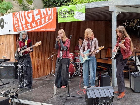 4 Jugendliche spielen auf der Bühne ein Lied mit Instrumenten und Gesang
