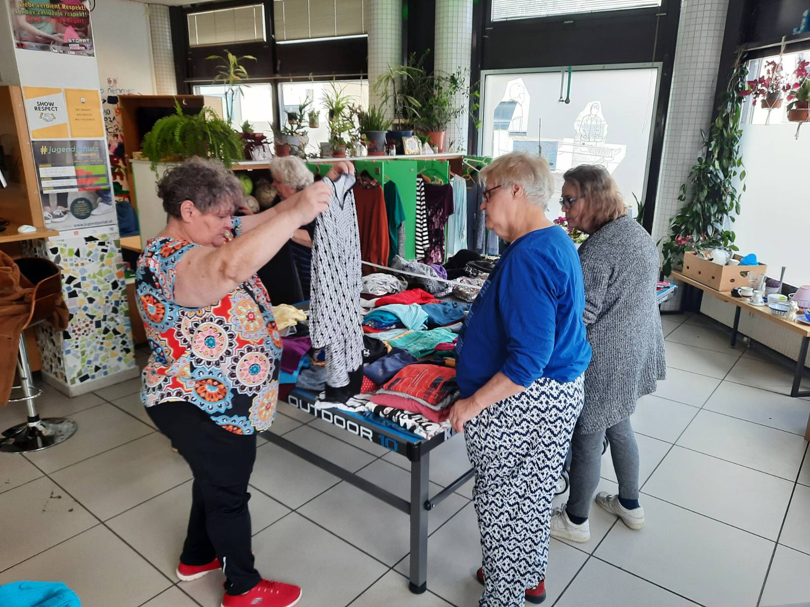 Frauen* betrachten Kleidung um einen Tisch
