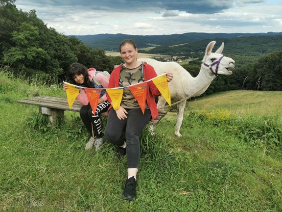 zwei Mädchen in der Natur mit einem Alpaka