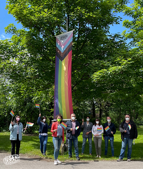 Mitarbeiter_innen vor Regenbogenflagge bei der Zentrale